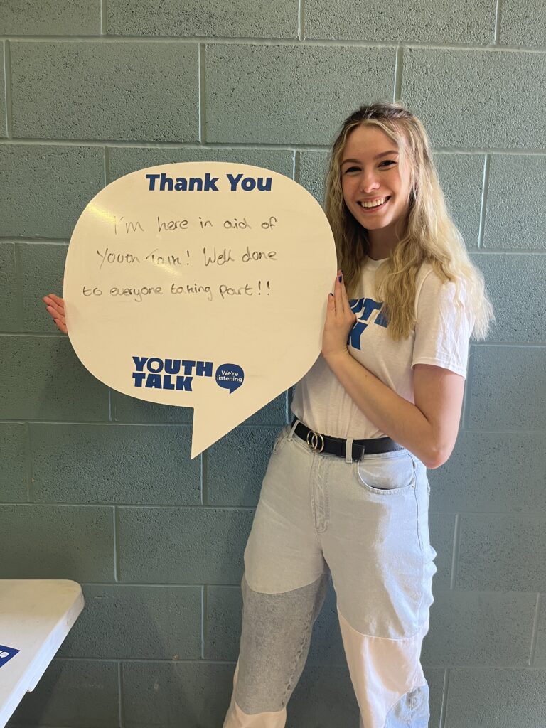 Rosie holding a speech bubble shaped whiteboard that reads: 'I'm here in aid of Youth Talk! Well done to everyone taking part.'