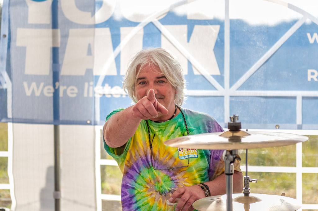 A man sitting at a drum kit and pointing into the camera. A Youth Talk banner is in the background.