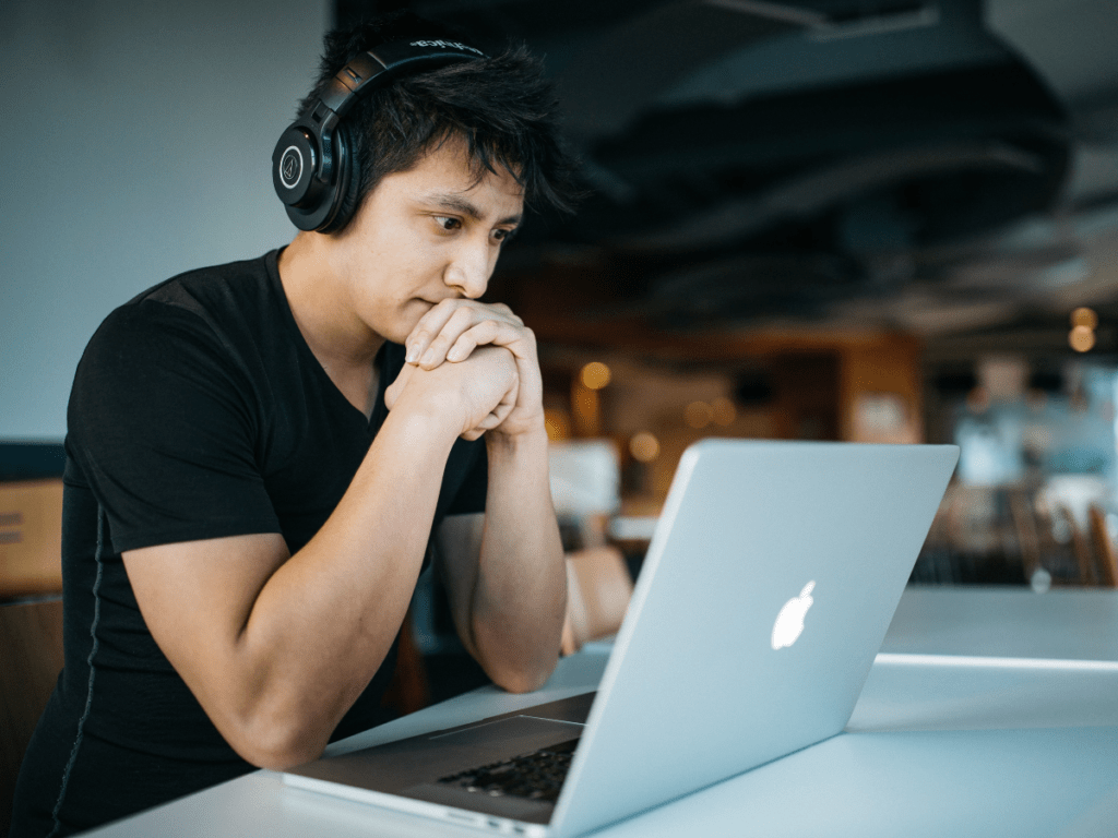 A young person with headphones on at a desk on their laptop.