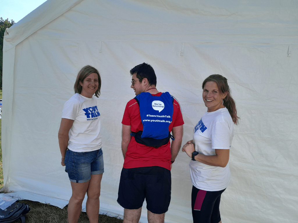 A picture from the St Albans Half Marathon in June. Two members of Youth Talk's fundraising team smiling at the camera. One runner has their back turned showing a Youth Talk vest.