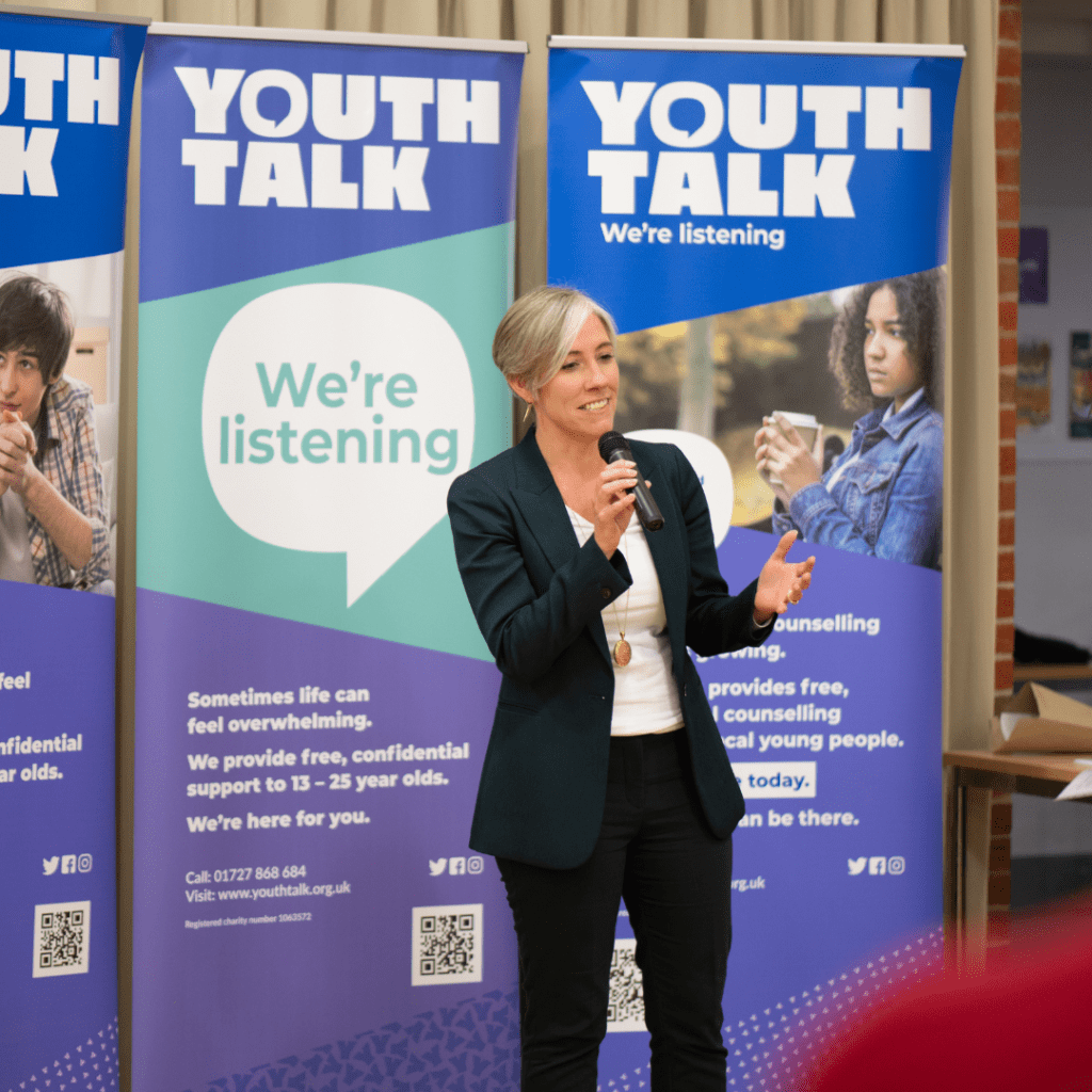 Daisy Cooper speaking at Youth Talk's 25th anniversary in front of pop-up Youth Talk banners